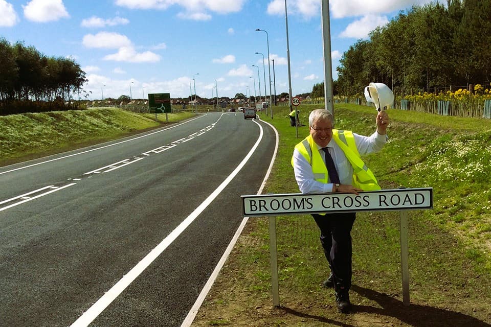 A man in a hard hat stood next to the brooms cross road sign